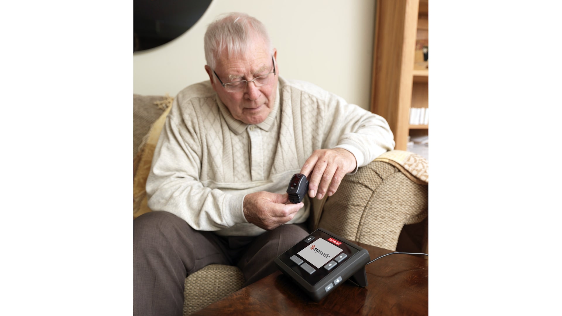 A senior uses a pulse oximeter. He is sitting on a couch at home.