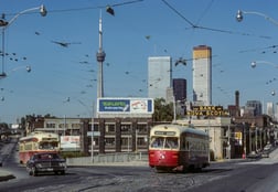 Photo from 1975 of two streetcars coming to a corner. The Toronto skyline is visible, including a clear view of the CN tower.Queen & King