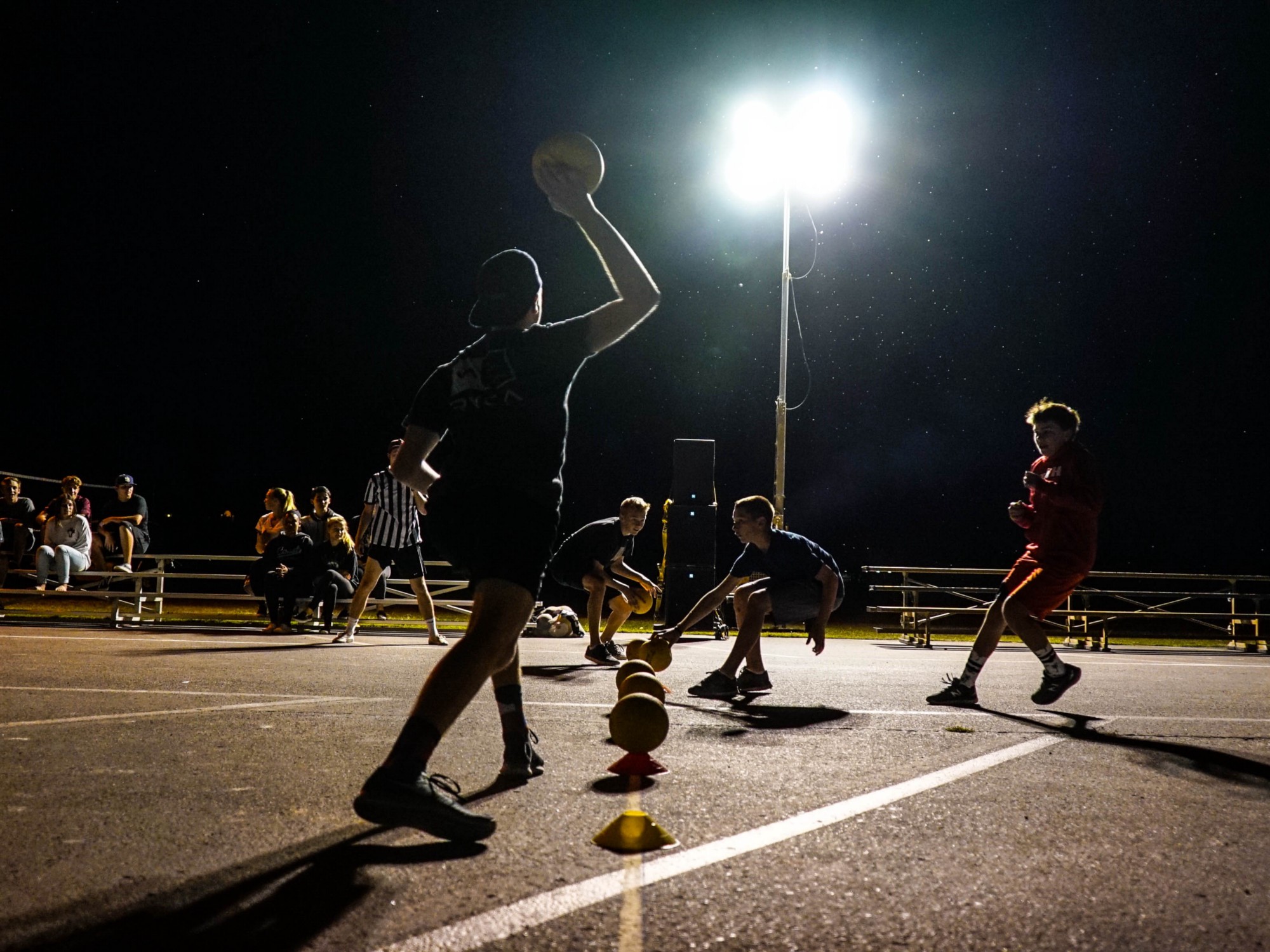 Players backlight with multiple balls on a dark court, it is unclear what game they're playing.