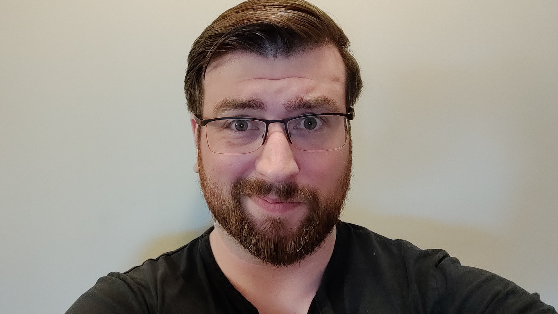 Brent Lintner is wearing glasses and a black shirt, and standing against a white wall.