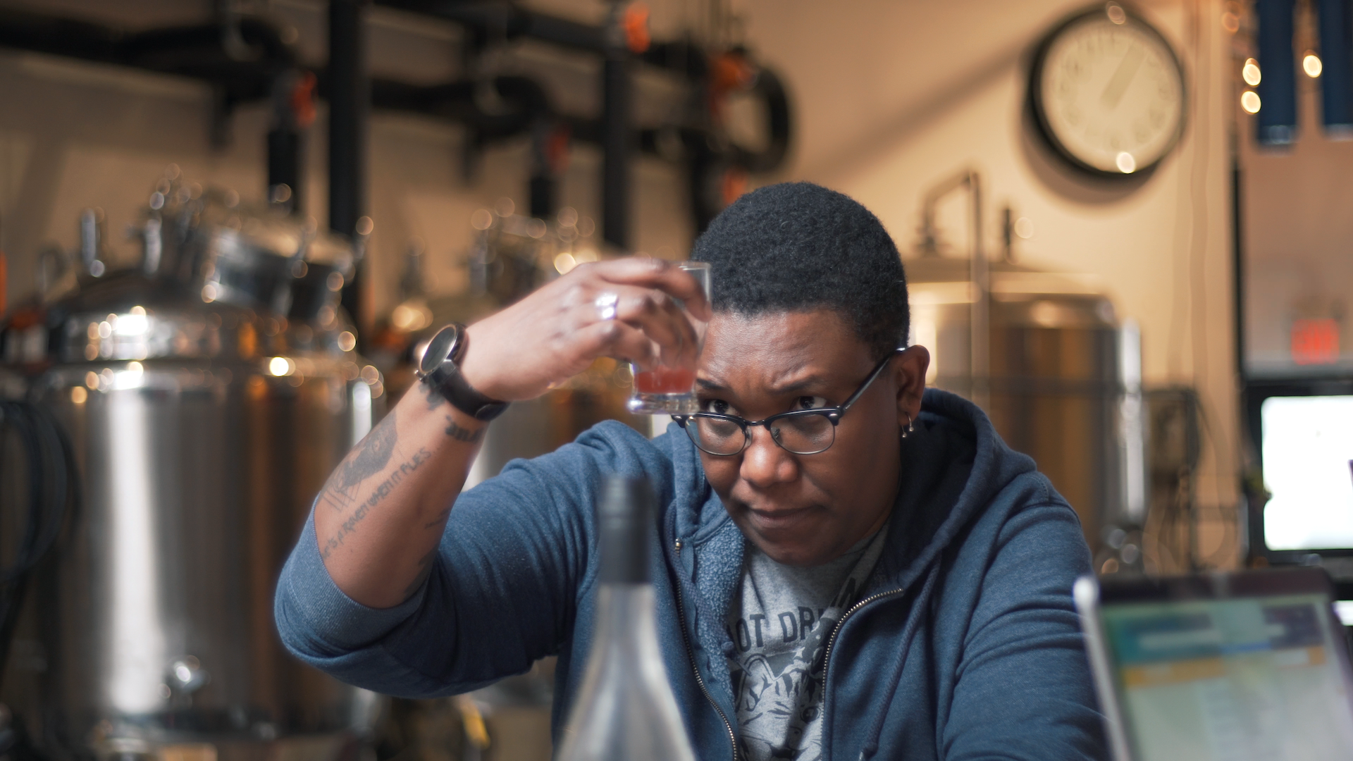 Ren Navarro sits in a brewery. She's holding up a glass and looking at the amber liquid in it.