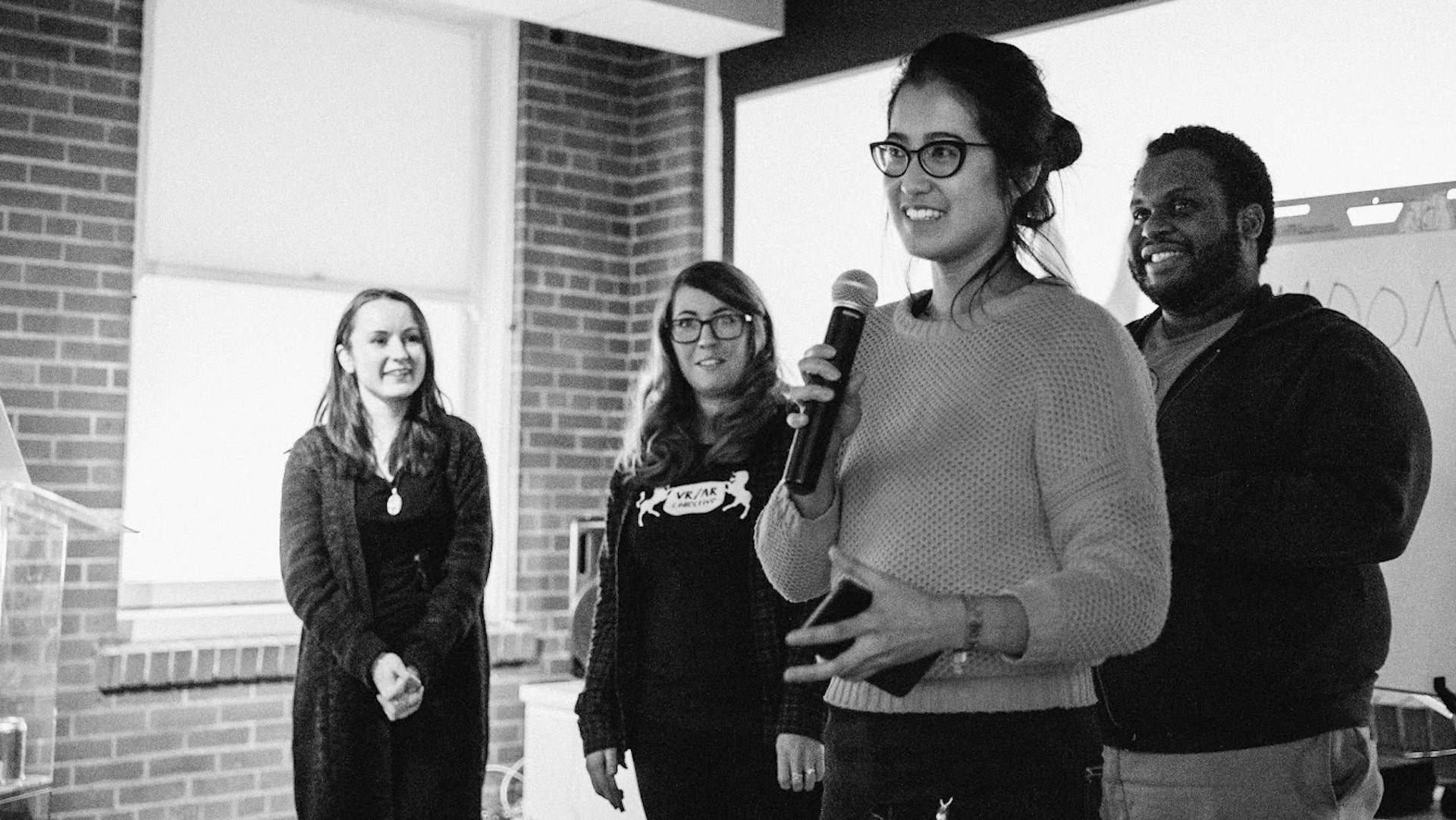 Di Dang is talking into a microphone while a group of people standing behind her look on.