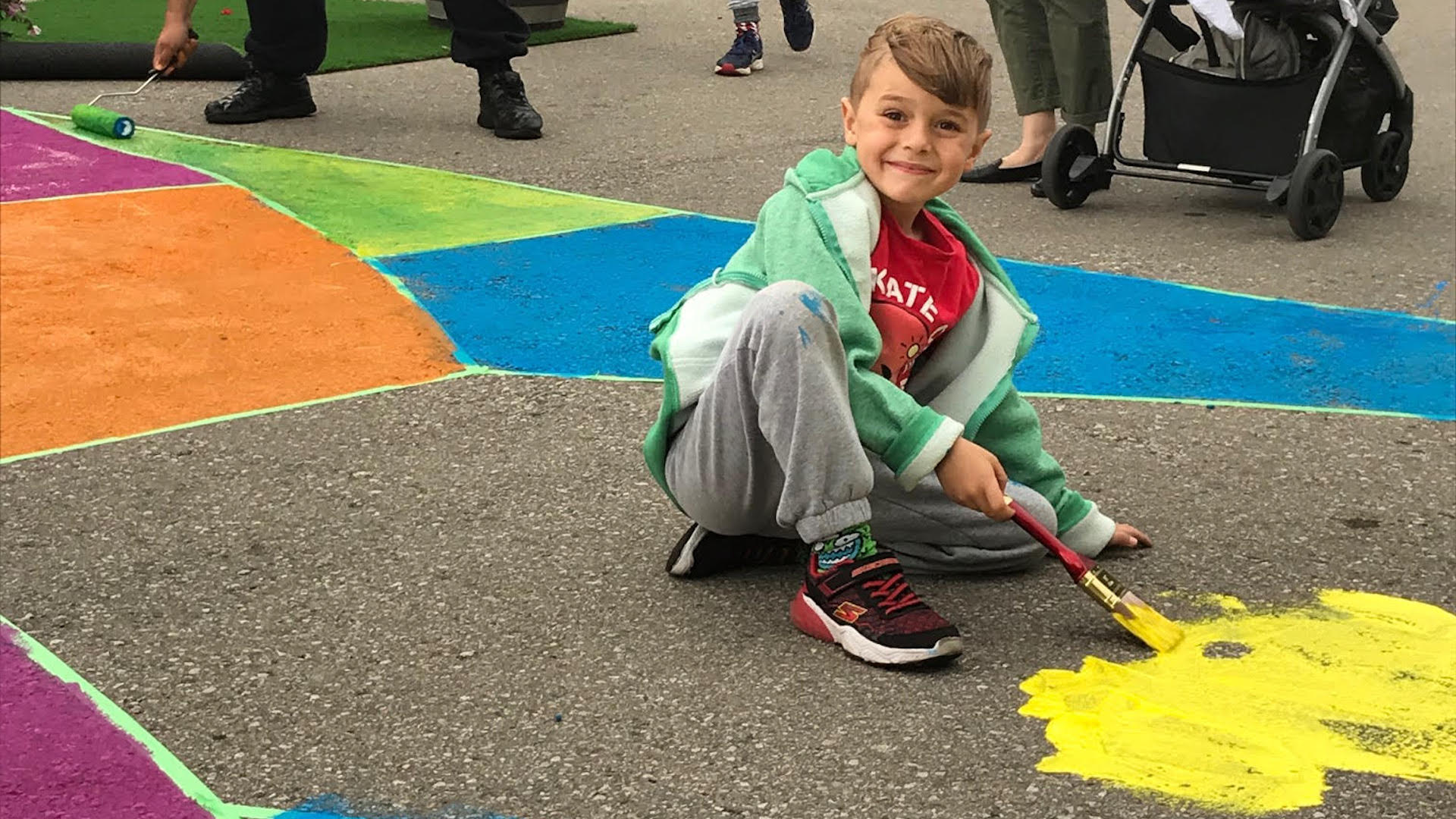 A boy smiling as he paints a mural on a road with other families