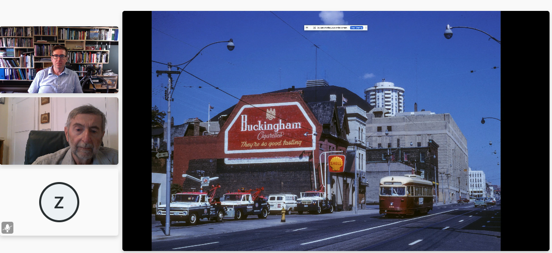 A screenshot of Brian Doucet and Michael Doucet showing an old photograph of a streetcar beside a building with a large cigarette ad painted on it.