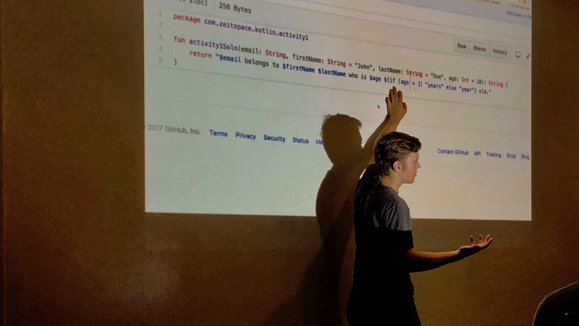 A presenter points to Kotlin code on a projector screen