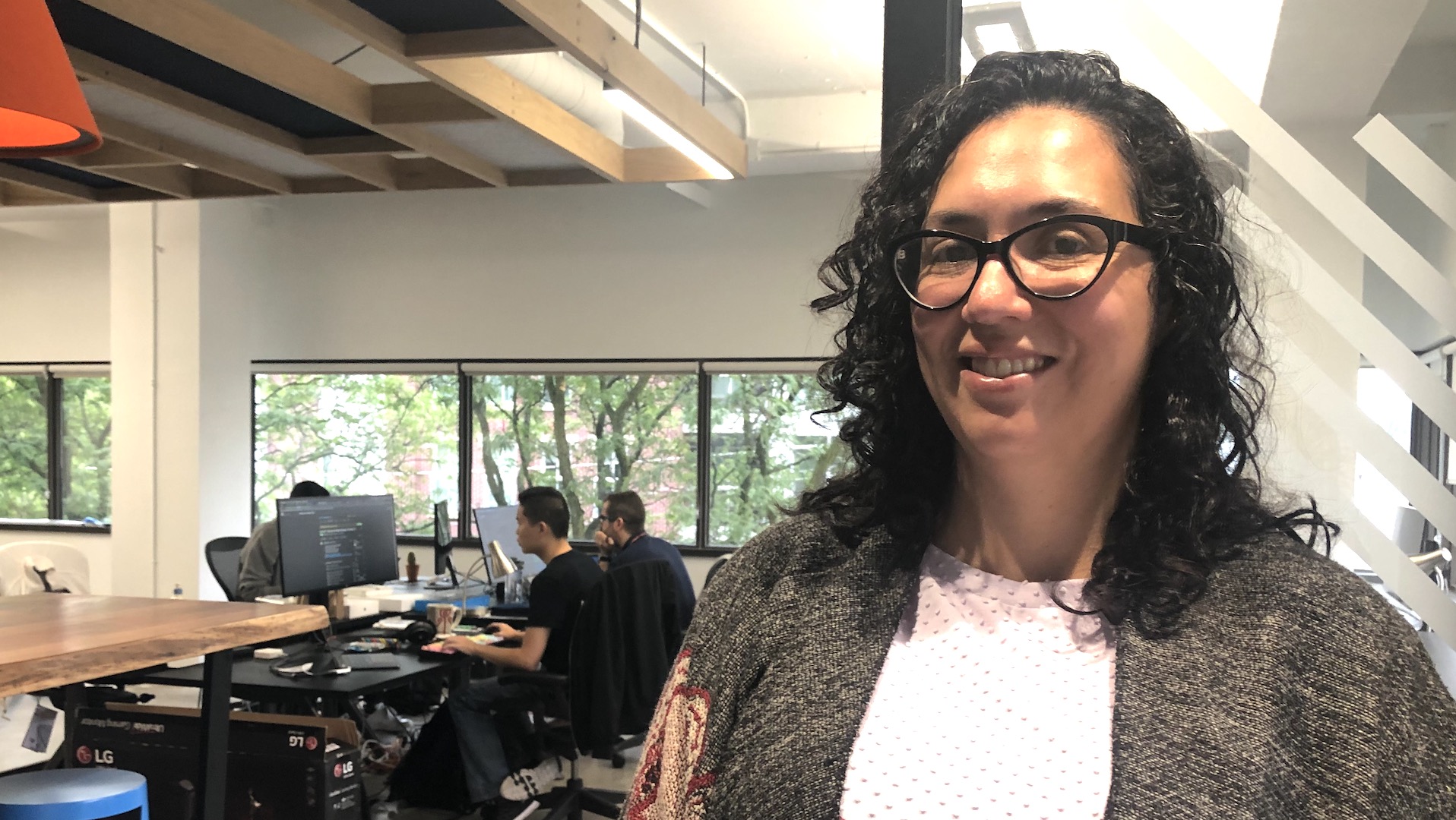 Kelly Pedro stands in the Zeitspace office while software developers work in the background.