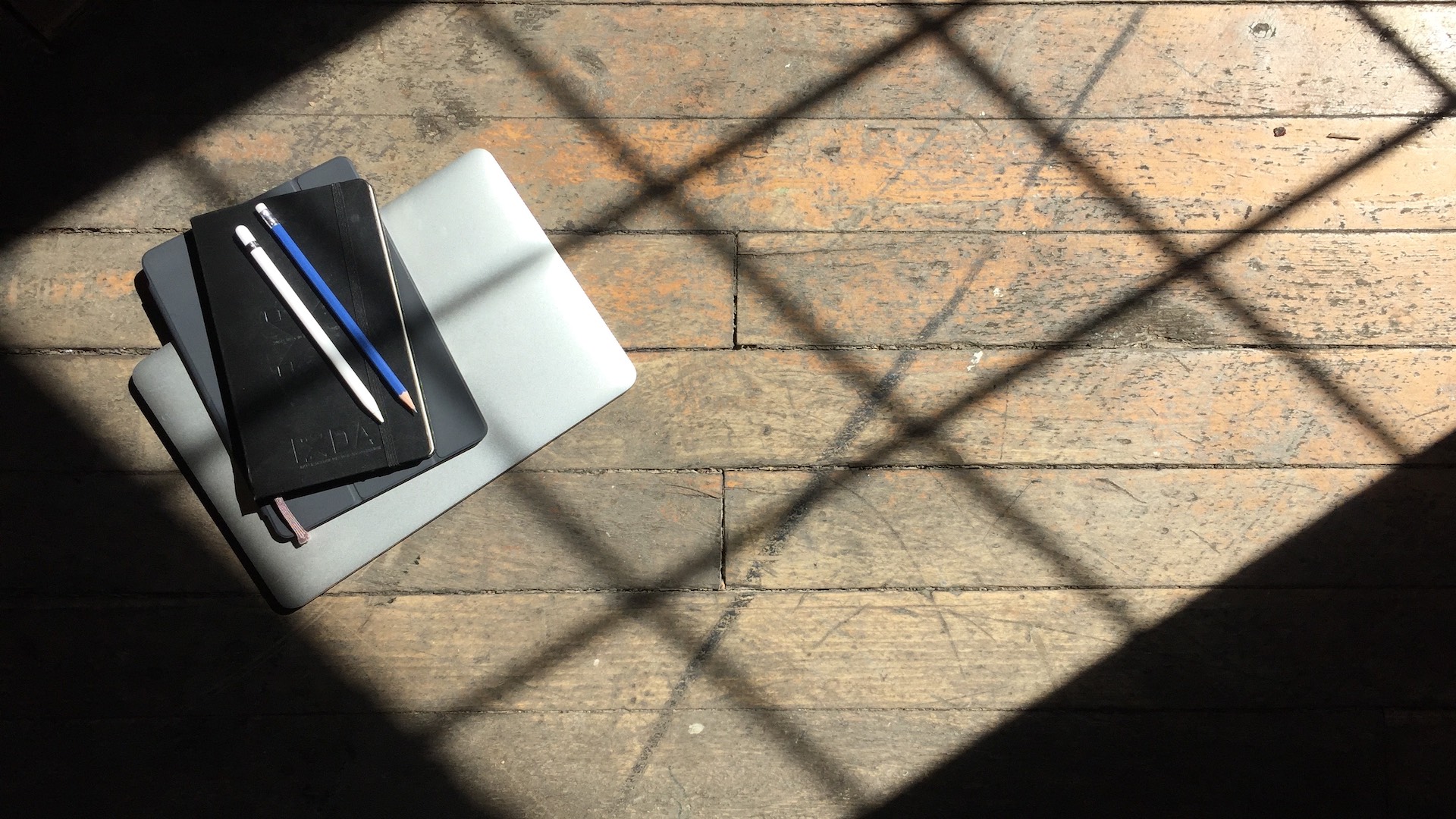 A notebook and laptop sit on a wooden floor