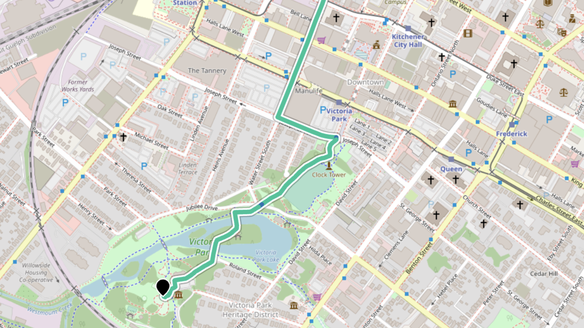 A map of Kitchener Ontario, with a green line representing a cycling route. The line enters at the top of the map and ends by a large black marker in Victoria Park.