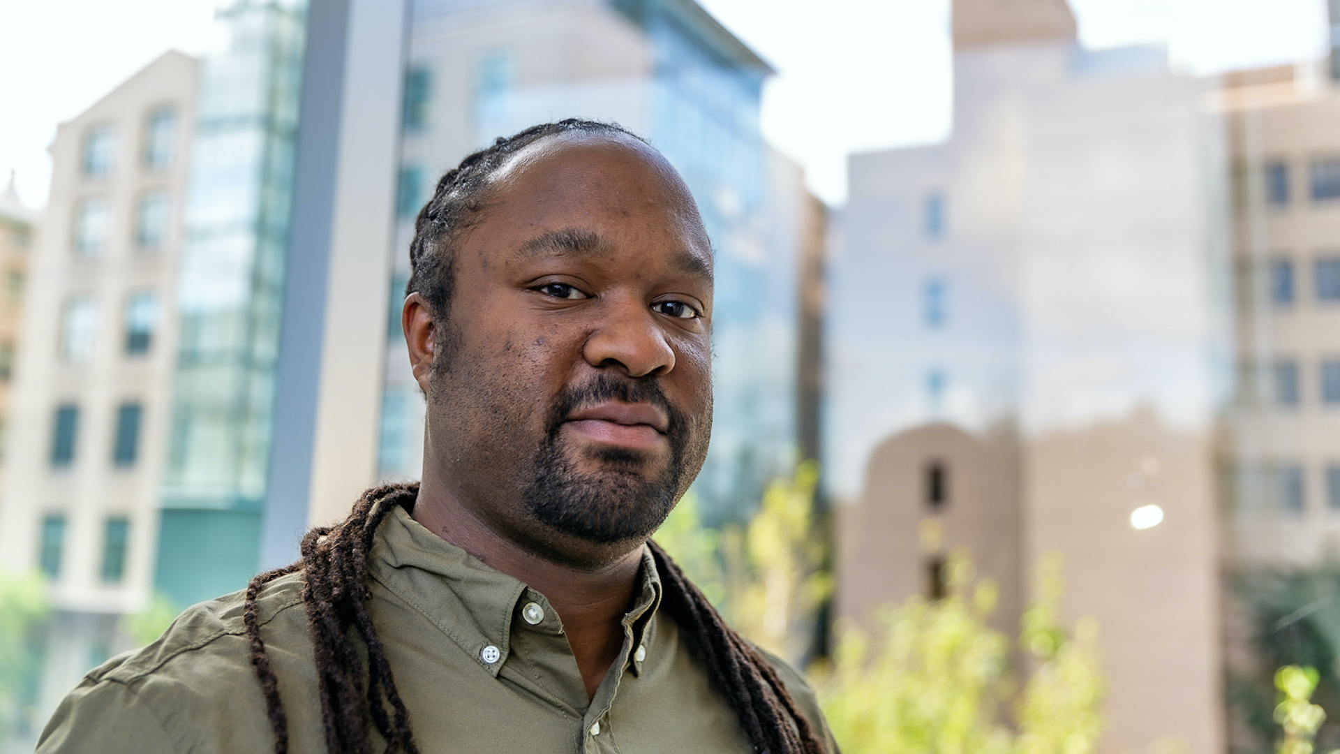 Patrick Carrington stands in front of a window. There are high-rise buildings in the background. 