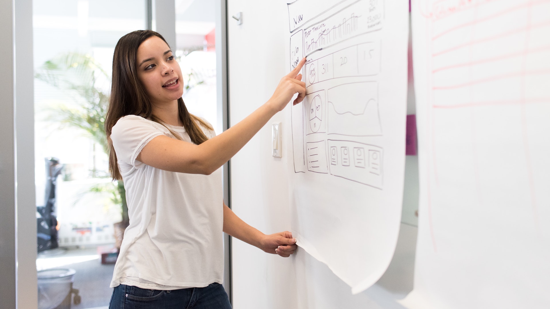 A person points at a chart on a large, hanging white sheet of paper.