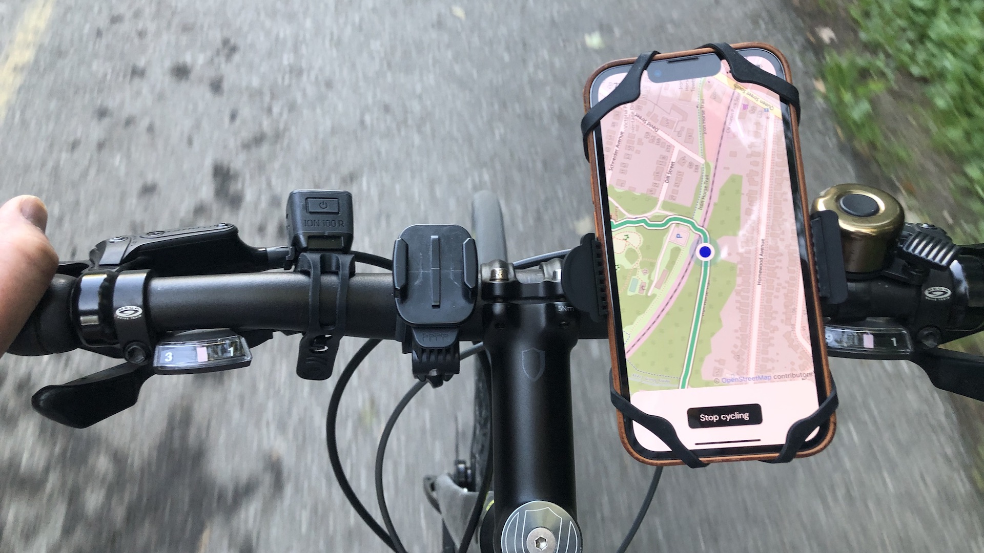 A bicyclist's view looking down at a phone mounted on bike handlebars. The phone's screen shows a map with a marked route on it.