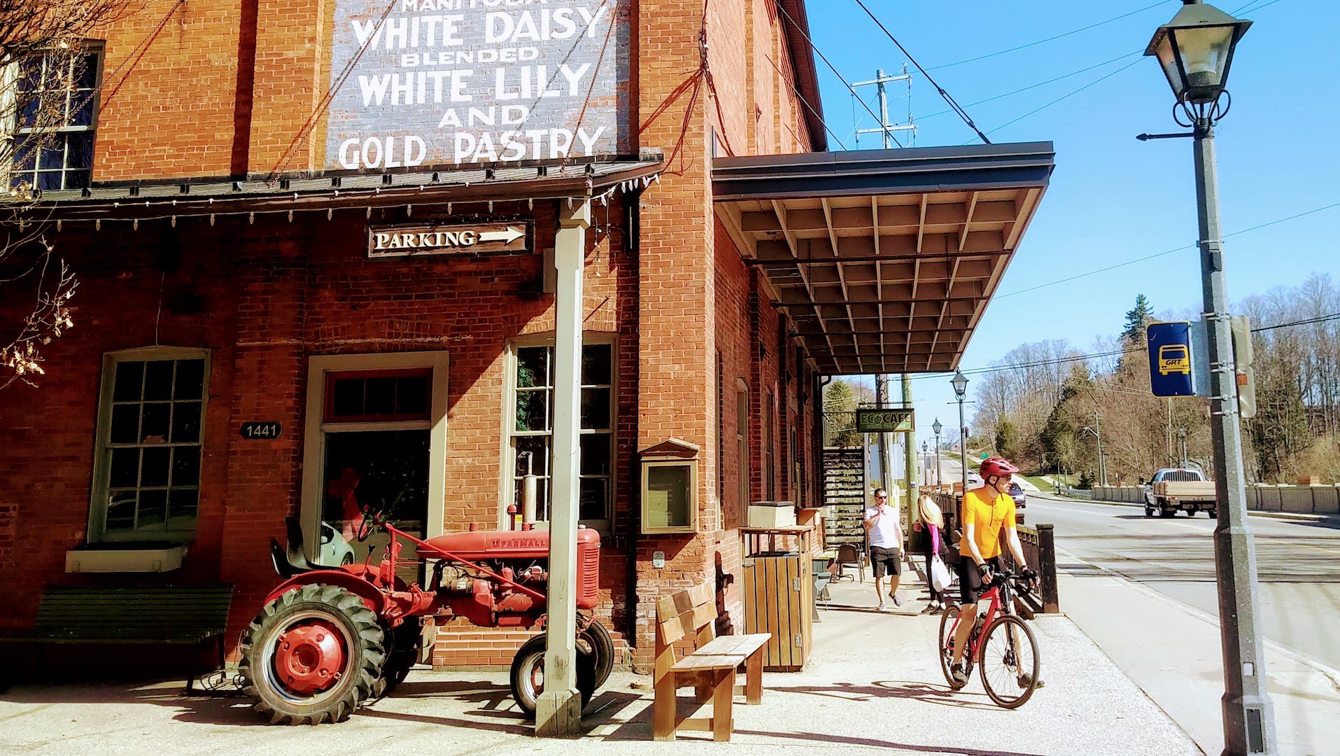 A red brick store There's a red farm tractor in the left foreground, and a cyclist in the right foreground.