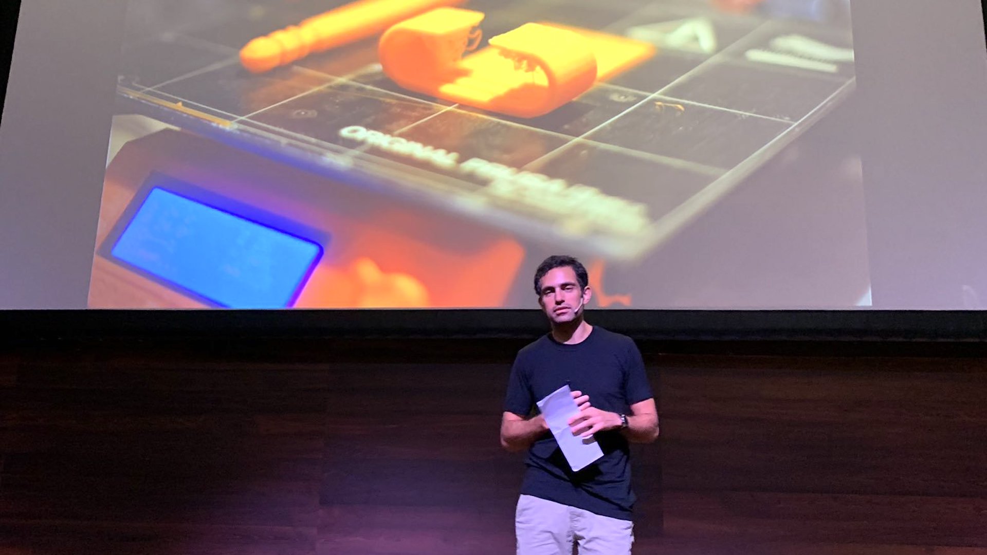 Tarek Loubani on-stage in-front of an image of a 3D Printer he uses to improve battlefield medicine