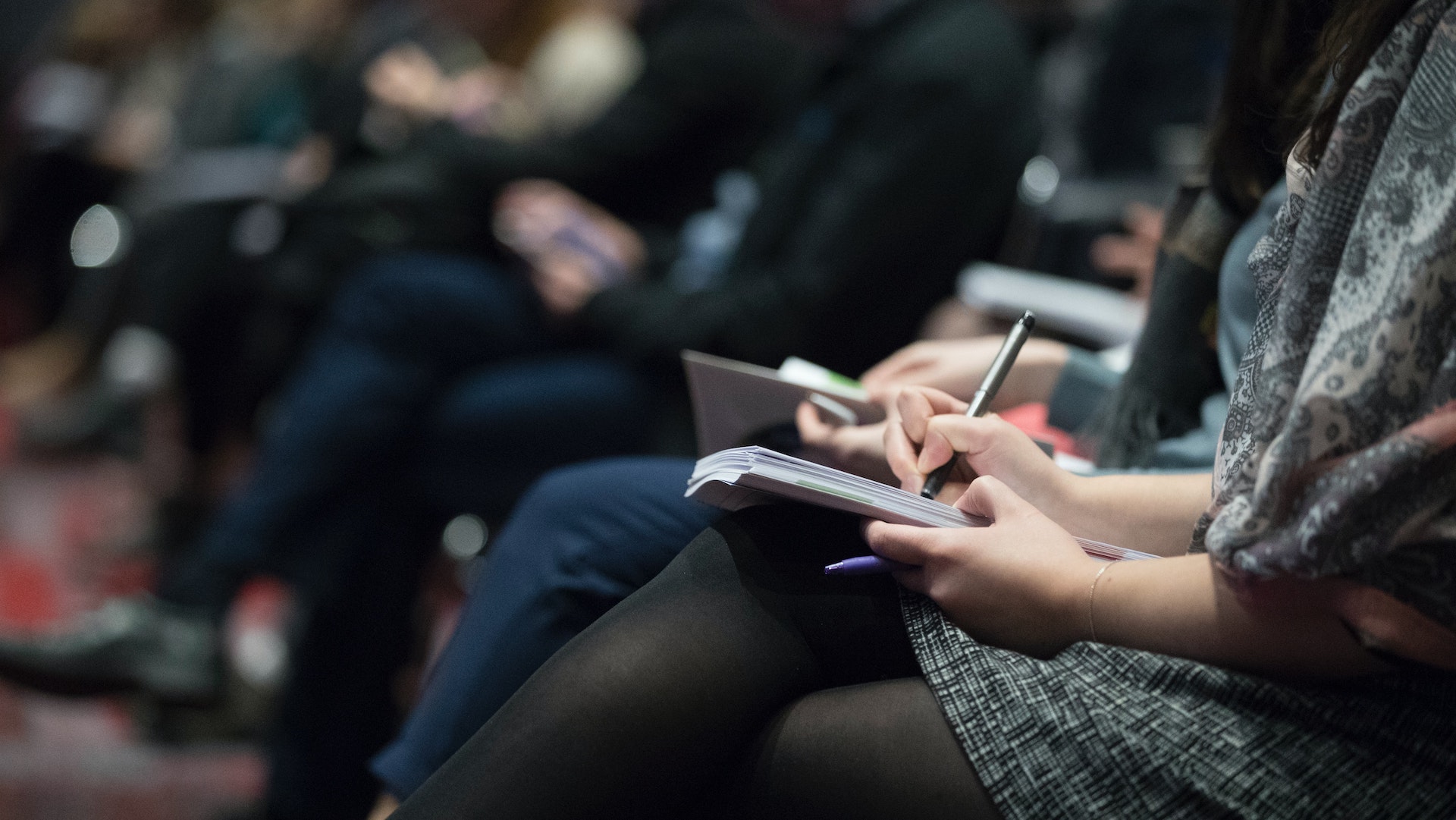 People sitting in a row taking notes in a notebook.