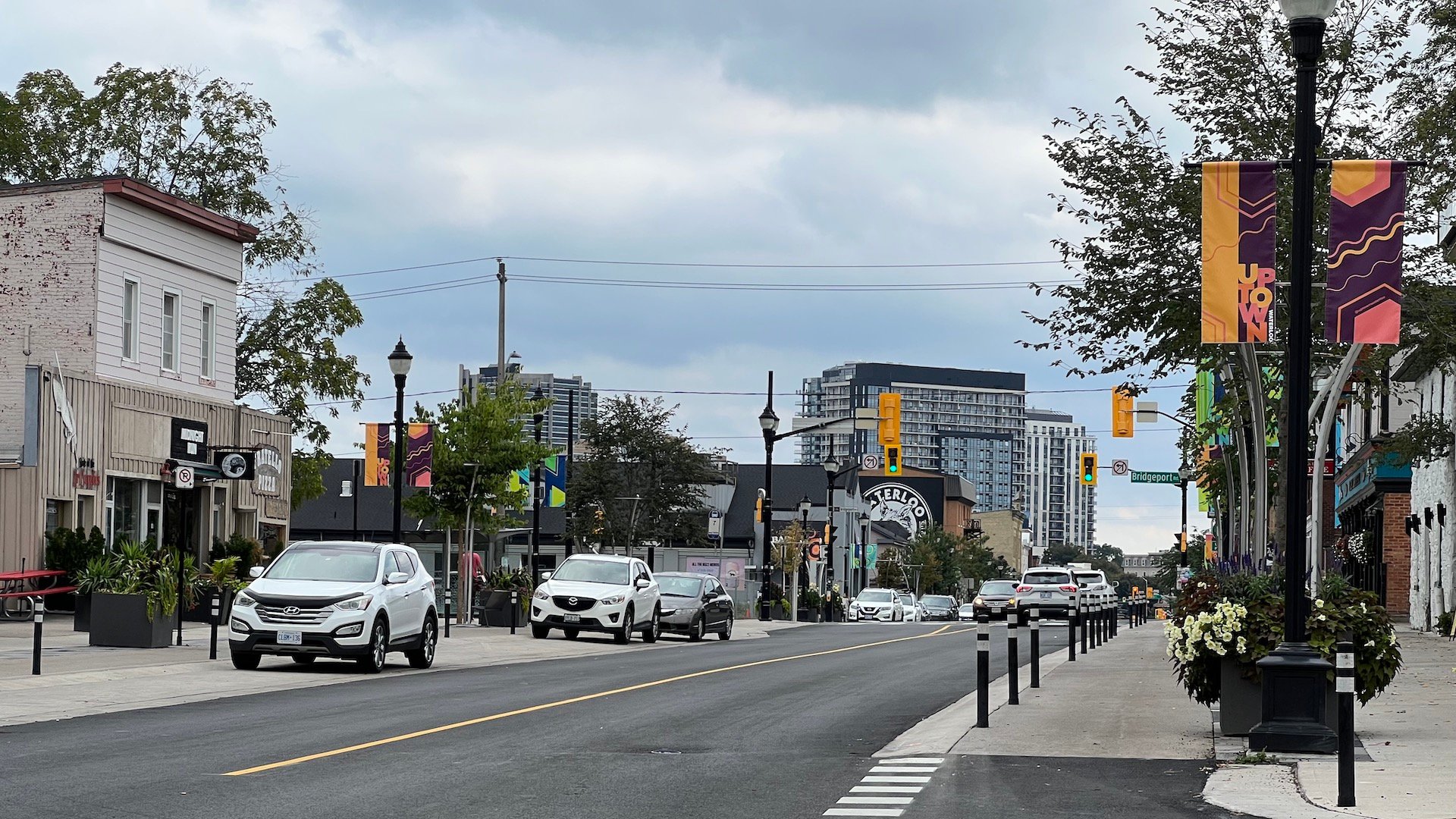 An urban street scene with cars parked at the side of the street. Between the street and the sidewalk there is a raised cycleway.