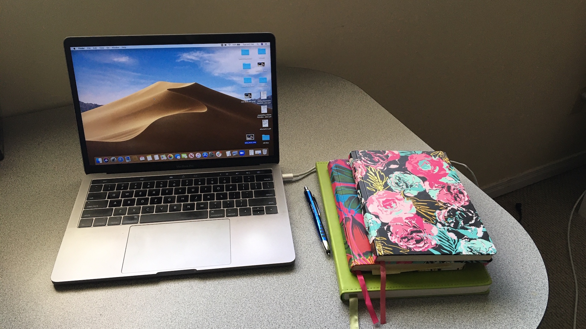 An open laptop on a grey desk with three notebooks stacked next to it.