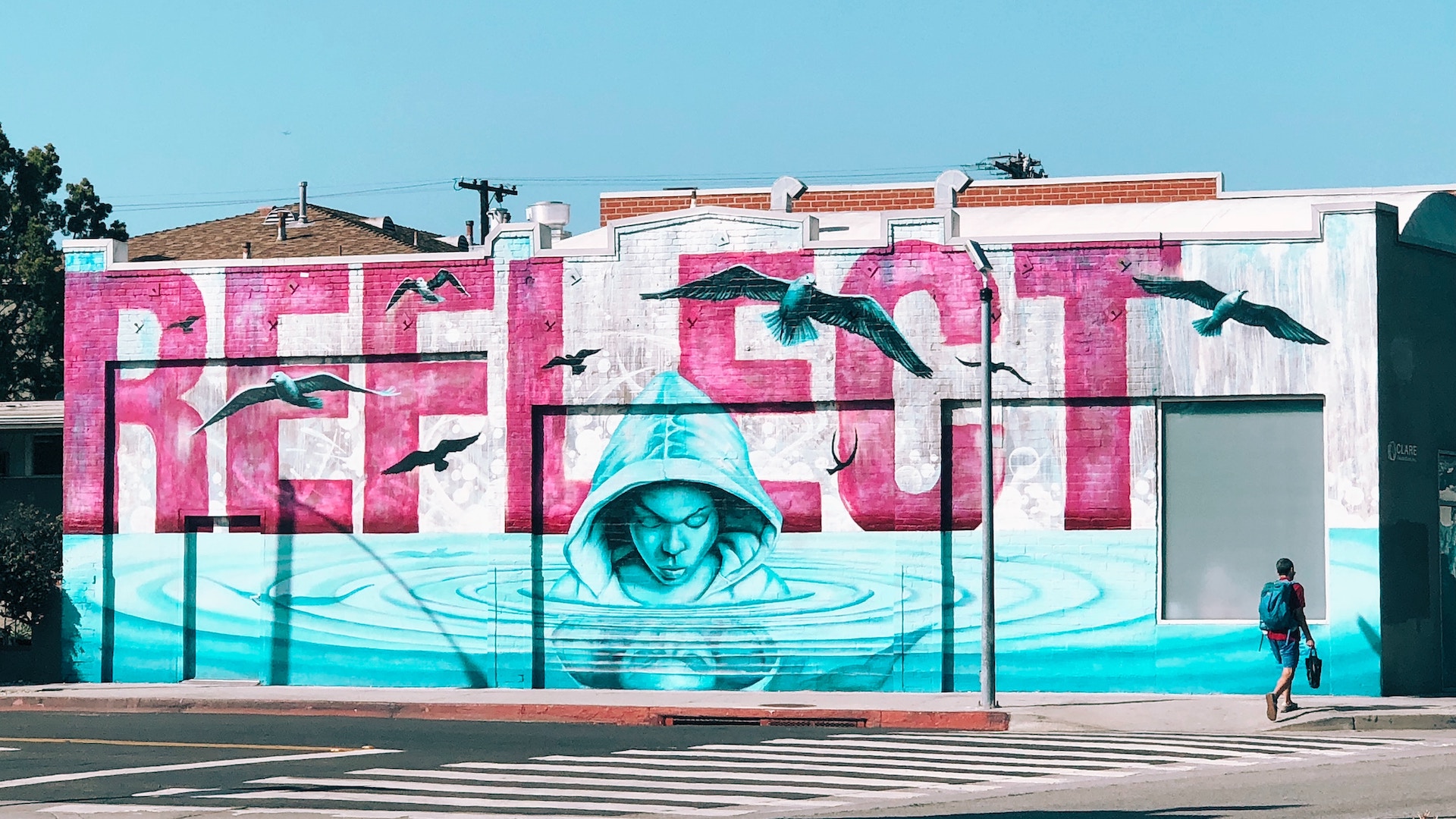 A pink and blue mural on the side of the building that features a person looking into rippling water with the word  'Reflect'