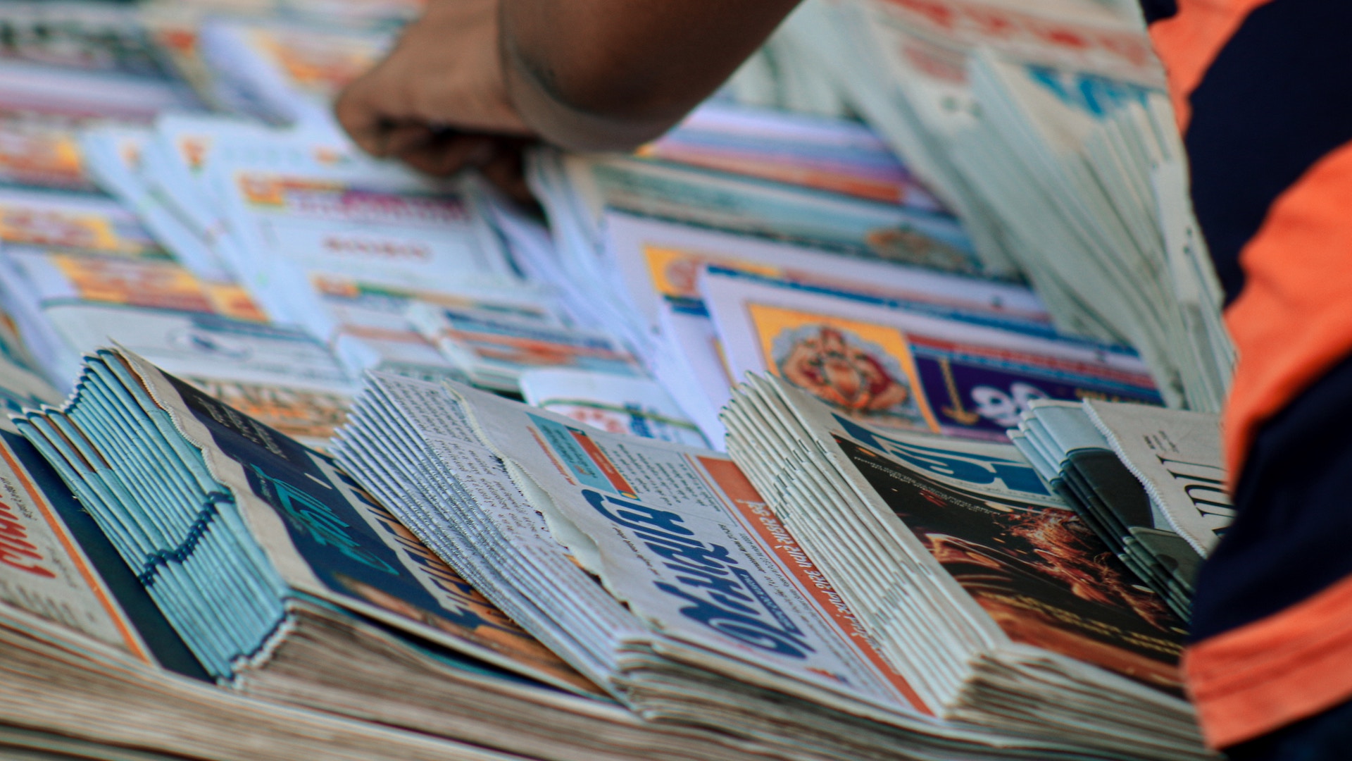 hands sort through piles of different newspapers