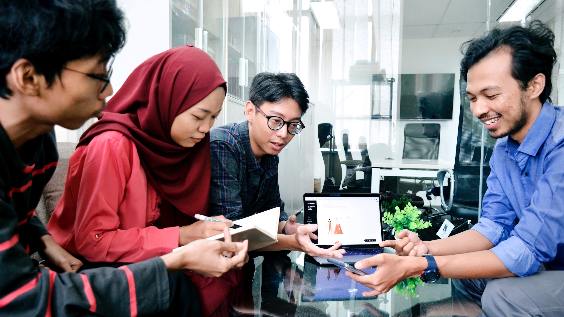 Four people sit around a desk. One is taking notes. 