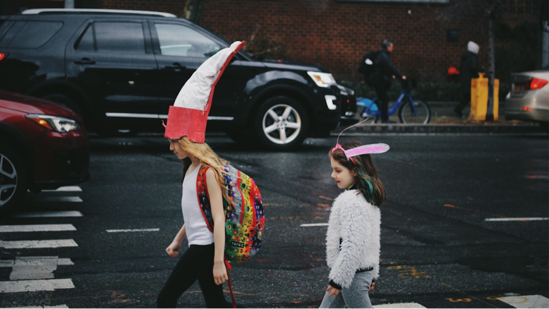 Two girls walking on a sidewalk as a car drives by.